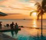 a glamorous beach resort at sunset, featuring elegantly dressed travelers enjoying cocktails by the crystal-clear ocean, with vibrant colors of the sky reflecting on the water.