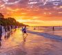 a vibrant sunset illuminates a lively beach where travelers, dressed in colorful attire, joyfully bask in the moment after an exhilarating safari adventure in the background.